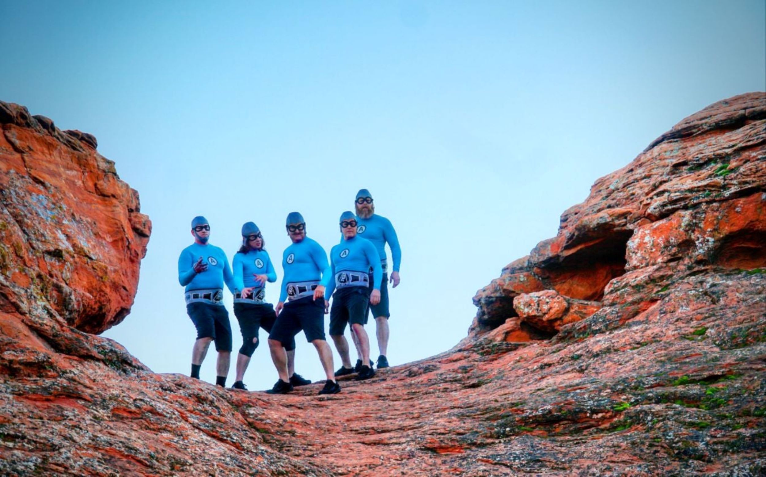 The Aquabats! strike a pose in their signature blue costumes while standing on top of a canyon.