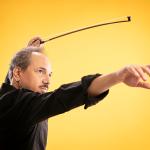 Violinst Luca Ciarla gesturing with his bow, on stage in front of a yellow background